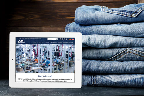 Stapel Jeans neben einem Tablet, das eine Webseite über Textilproduktion von Bizoceanstar GmbH anzeigt