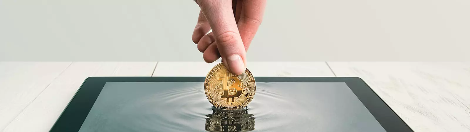 Hand, die eine Bitcoin-Münze in ein Tablet-Display taucht, das wie Wasser wirkt