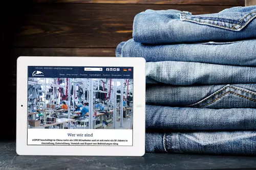 Stapel Jeans neben einem Tablet, das eine Webseite über Textilproduktion von Bizoceanstar GmbH anzeigt