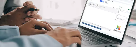 Zwei Personen, die an einem Laptop arbeiten, der die Joomla-Benutzeroberfläche anzeigt, während eine Person Anweisungen gibt