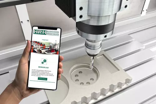 Person hält ein Smartphone mit der Website von HR Tools, im Hintergrund eine CNC-Maschine bei der Arbeit