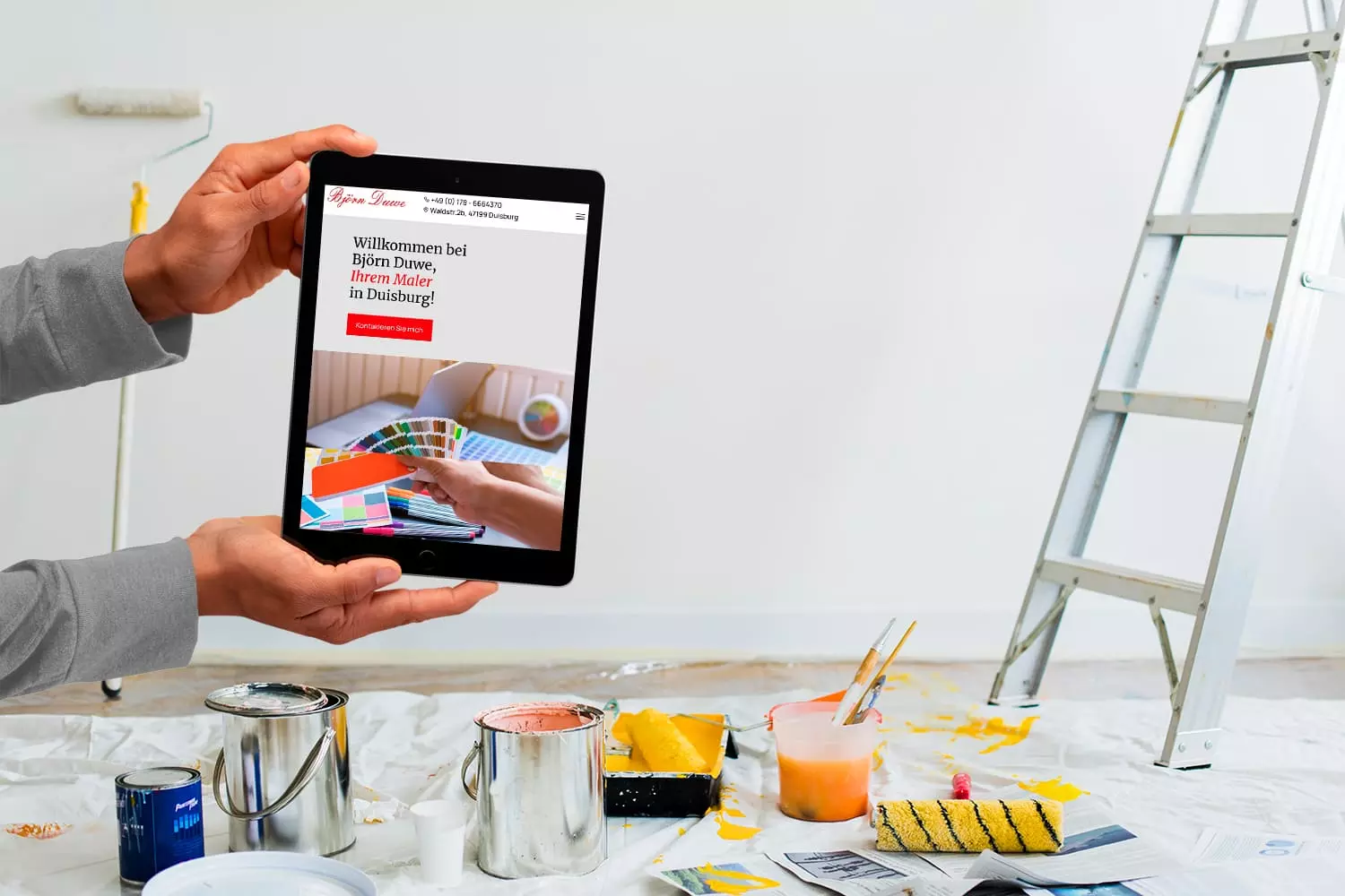 Person hält ein Tablet mit der Joomla Website eines Malerbetriebs in einem renovierten Raum mit Malutensilien