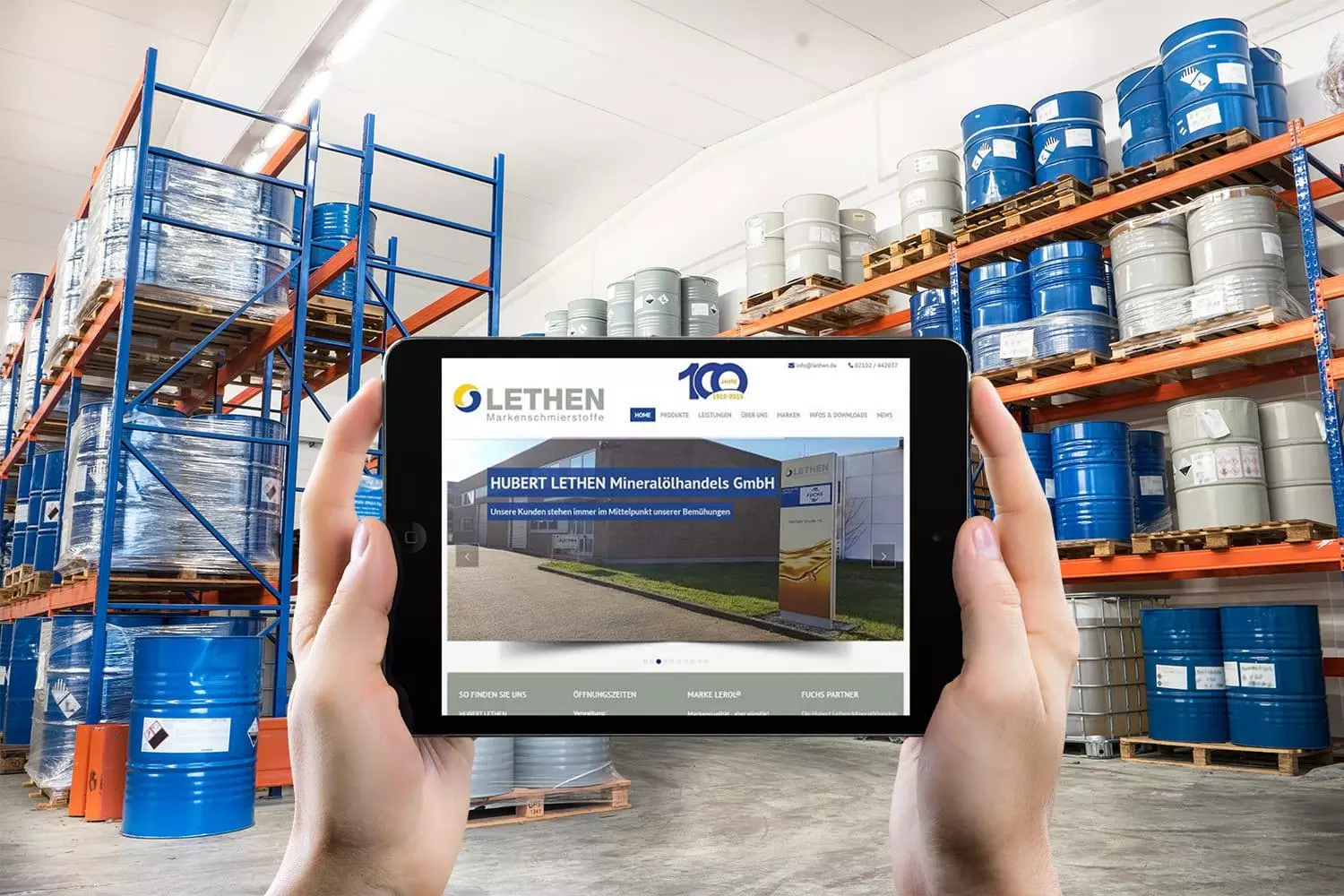 Person hält ein Tablet mit der Website der Hubert Lethen Mineralölhandels GmbH, im Hintergrund ein Lager