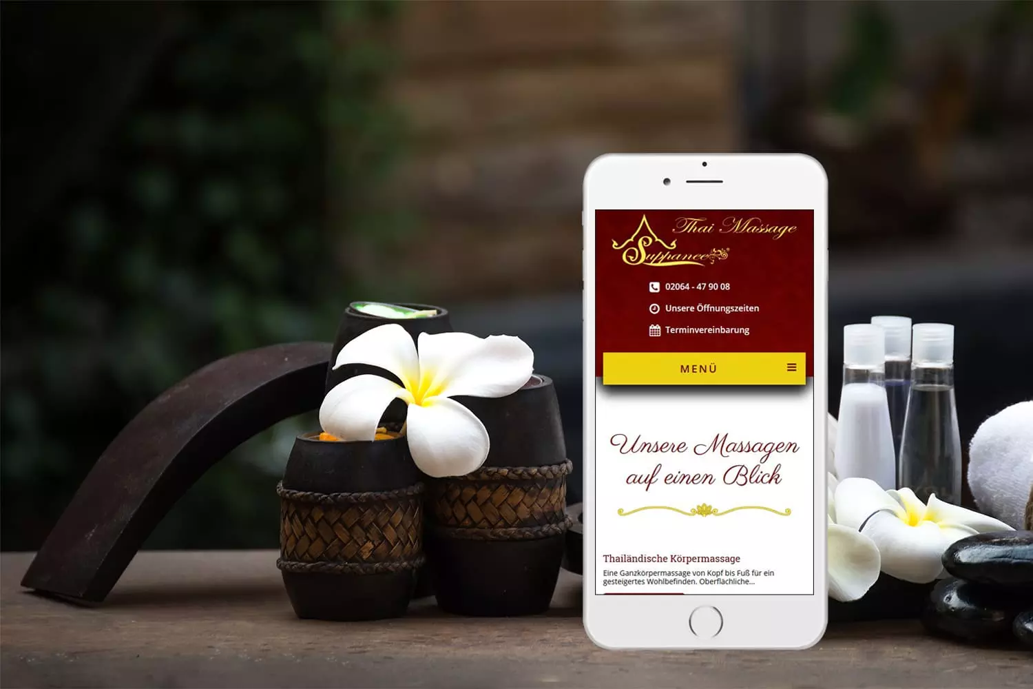 Smartphone mit der Thai Massage Suphanee Webseite, neben traditionellem Massagezubehör und einer Blume