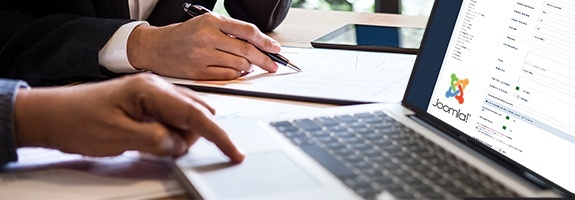 Zwei Personen bei einer Joomla Beratung, während eine Person auf einem Laptop arbeitet, der die Joomla-Benutzeroberfläche anzeig