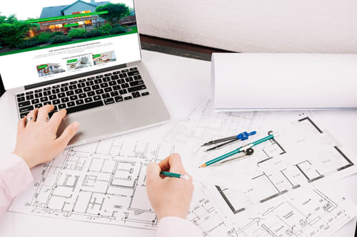 Joomla Webdesign für die KP Constructio Immobilien-Website in Obertshausen – Professionelle Immobilienpräsentation Person arbeitet an einem Laptop mit der Website von KP Constructio Immobilien, umgeben von Bauplänen und Zeichnungen