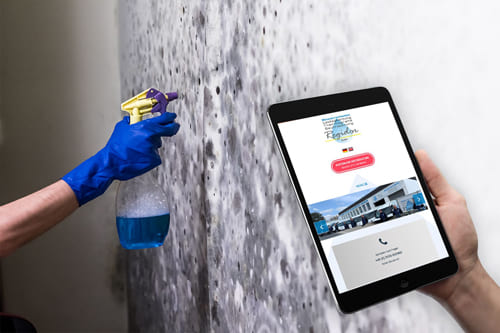 Joomla Webdesign für die Regidor GmbH-Website in Ratingen – Professionelle Reinigungs- und Sanierungsdienste Person hält ein Tablet mit der Website von Regidor GmbH, während eine Wand mit einem Reinigungsmittel besprüht wird