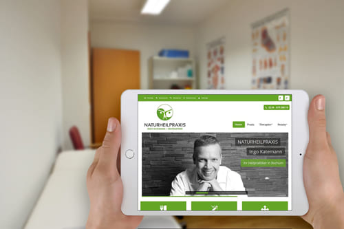 Joomla Referenz Webseite von Heilpraktiker Ingo Katemann in Bochum – Professionelles Webdesign für Heilpraktiker Person hält ein Tablet mit der Website von Heilpraktiker Ingo Katemann, im Hintergrund ein Behandlungsraum