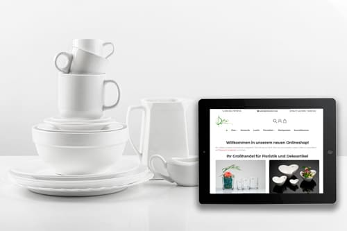 Referenz Onlineshop für Floristik- und Dekorationsartikel von Dekodom Tablet mit Dekodom Onlineshop neben gestapeltem Geschirr