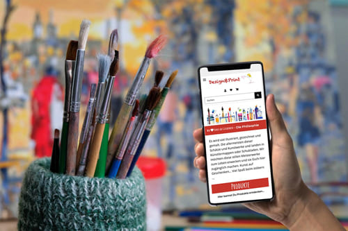 Referenz Onlineshop für Kunst und Designprodukte bei Design&Print Smartphone mit Design&Print Onlineshop neben Künstlerpinseln