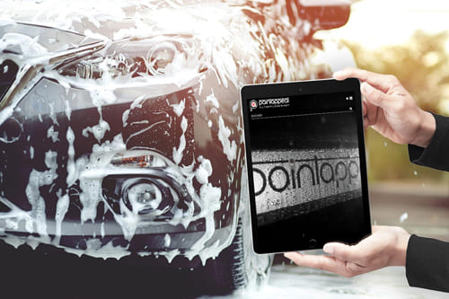 Referenz Onlineshop für Autopflegeprodukte von Paintappeal GmbH Tablet mit Paintappeal Onlineshop vor einem Auto in der Autowaschanlage